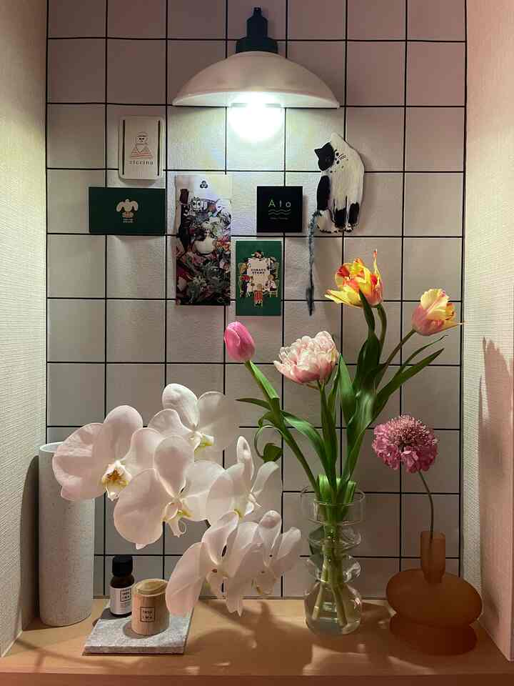 白いタイルと黒い縦横の線がある玄関、さまざまな花や植物が木製の棚に配置され、温かみのある雰囲気のインテリア