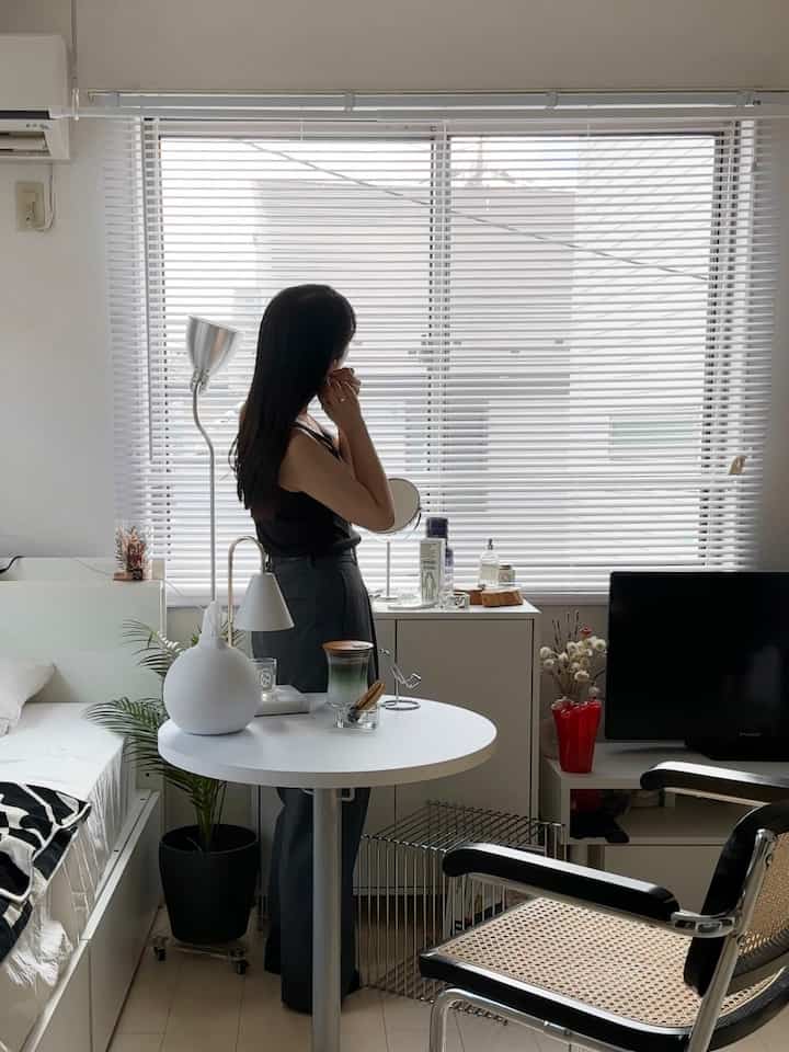White and black dominated studio bedroom with a round table, chair, and storage cabinet, featuring a natural and cozy atmosphere