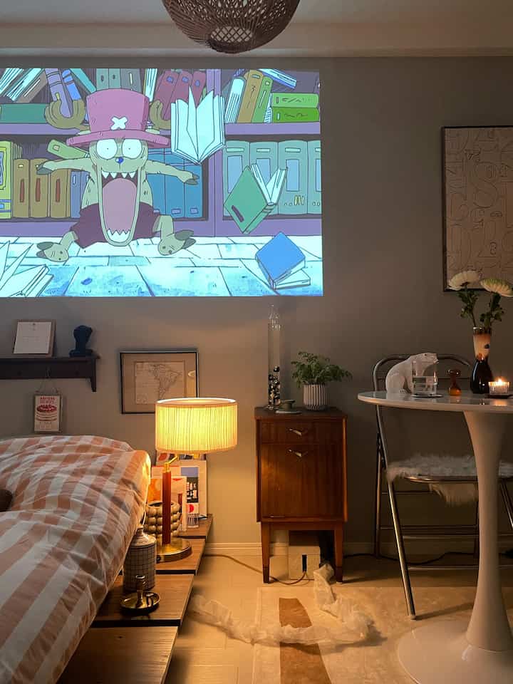 Cozy bedroom at warm night, featuring checkered bedspread, table lamp, and projector screen projection