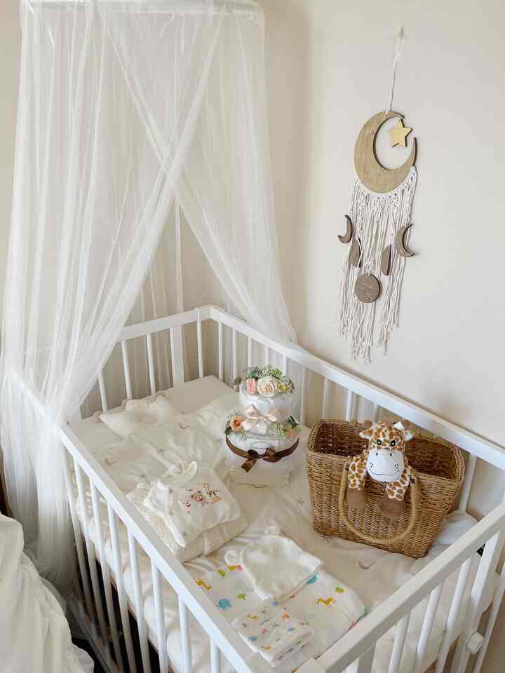 White and beige toned bedroom featuring a baby crib with a sheer canopy and rattan basket, creating a warm atmosphere.