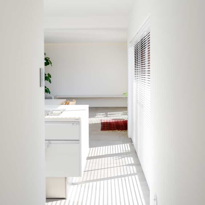 Natural modern white and brown kitchen and living space featuring smart blinds with bright sunlight, presenting a minimal and well-lit interior