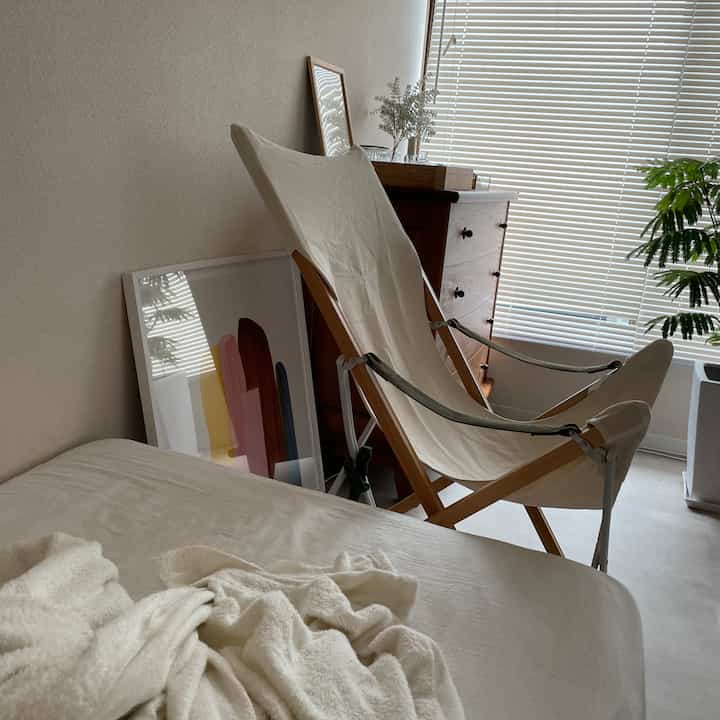 Natural-tone bedroom corner featuring a beige canvas armchair, vintage wooden dresser, and a plant creating a cozy atmosphere