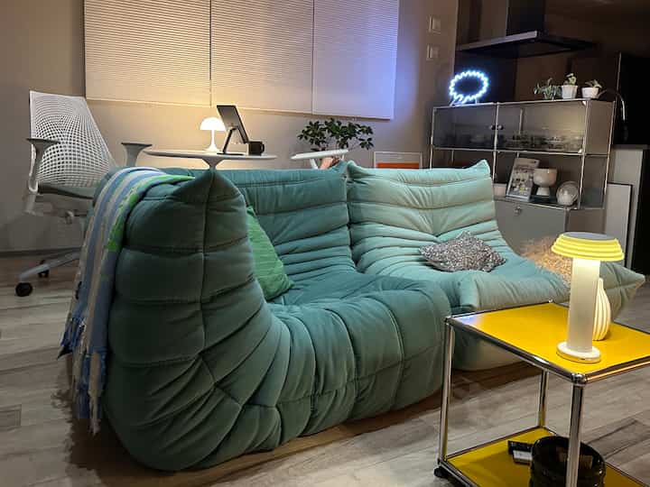 ティファニーブルーのソファとホワイトのオフィスチェア、イエローのサイドテーブルが配置されたモダンなリビング、柔らかなLED間接照明が雰囲気を演出