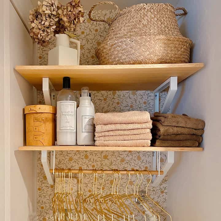 Natural-toned bathroom space featuring wooden shelves with neatly folded towels and storage baskets, creating a cozy atmosphere
