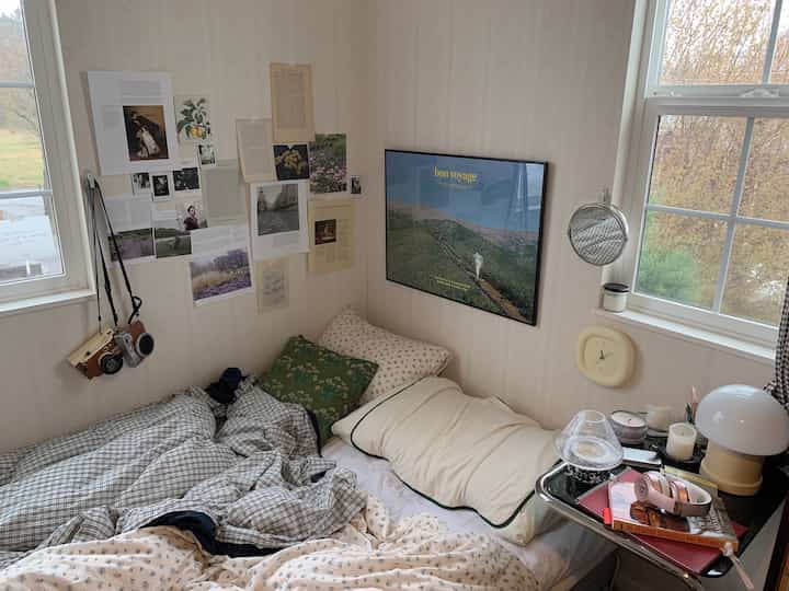 白を基調としたワンルーム寝室、居心地の良いベッドとヴィンテージ調のインテリアが配置された落ち着いた空間