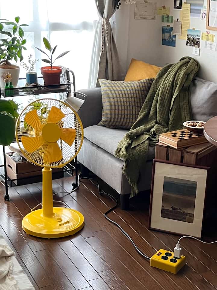 Bright wood-tone floor and gray sofa with a yellow fan and natural elements in a cozy living room space