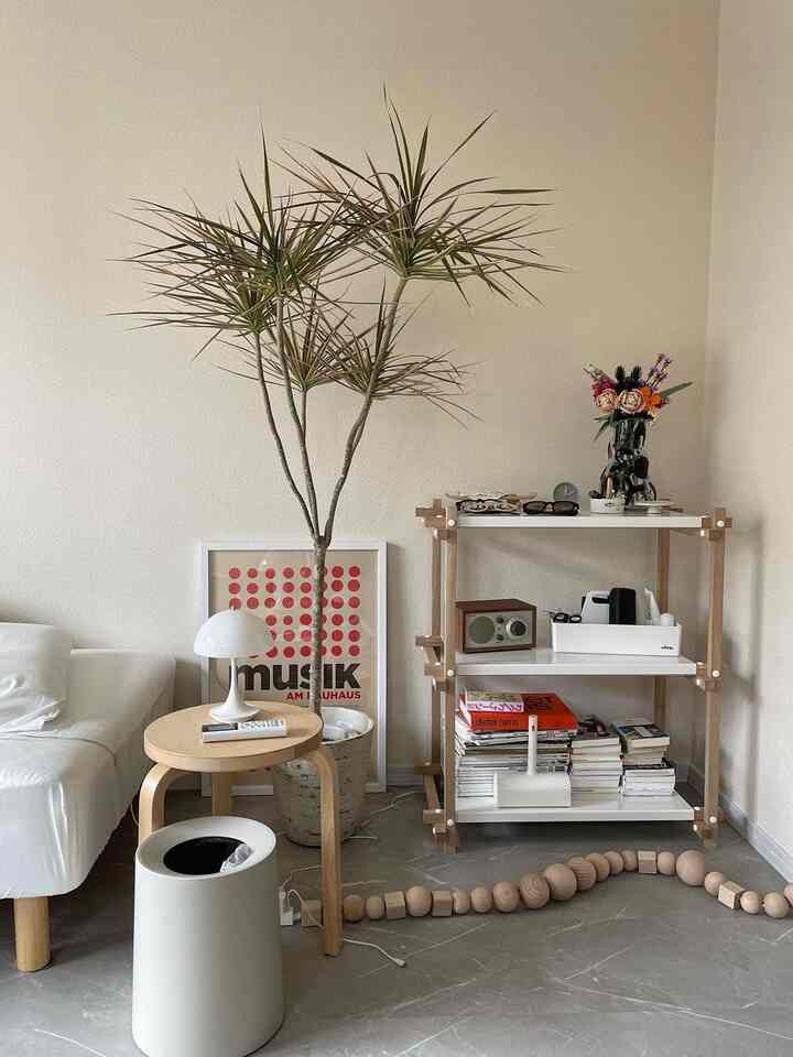 ナチュラルな色調のリビング、ホワイトのソファと観葉植物、木製のサイドテーブルと本棚が配置されたシンプルなインテリア