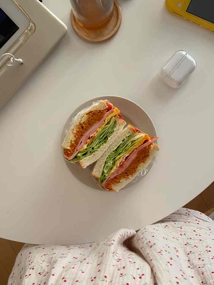 白を基調としたワンルームの丸テーブルにサンドイッチと透明なプラスチック容器が置かれた、すっきりとした雰囲気のインテリア