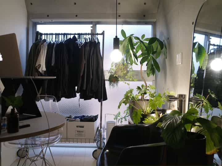 モノトーンとシルバーのワンルーム空間、窓際に服掛けと多様な植物が置かれたモダンなおうちカフェの雰囲気