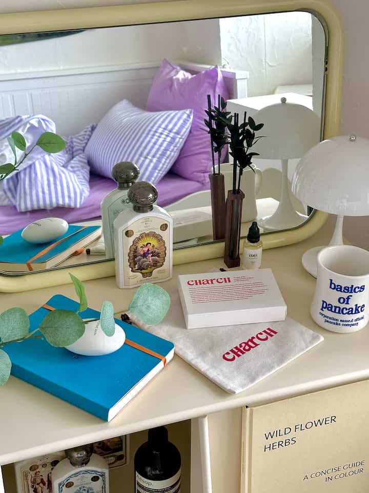 淡いベージュ色のテーブルにデコレーションアイテムとディフューザーが並ぶ寝室の鏡前空間