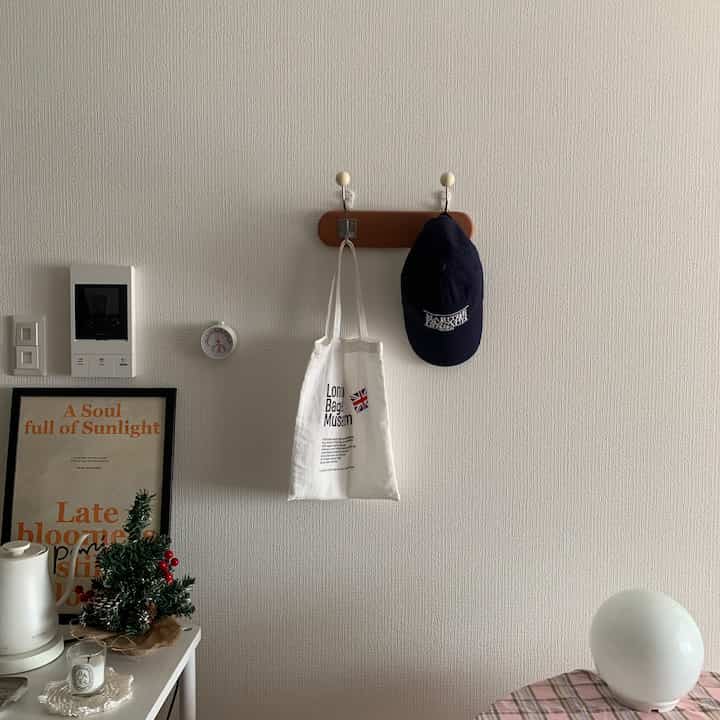 白い壁に茶色の木製ウォールフックが設置され、バッグとキャップ帽子が掛けられたシンプルな玄関のインテリア