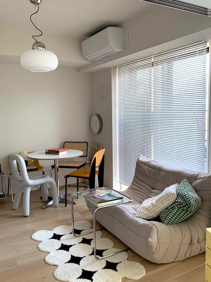 白い壁とベージュのソファが配置されたモダンなリビングルーム、丸いダイニングテーブルと多様な椅子が置かれた明るく清潔感のある空間