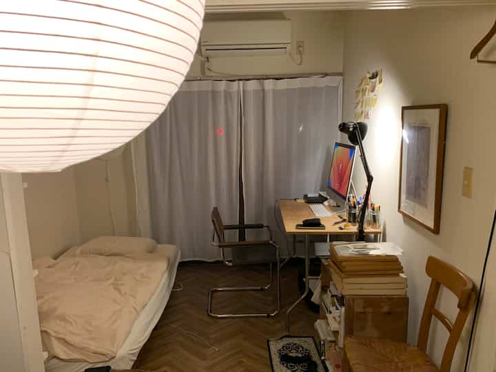 Ivory walls and wood-tone floor in a compact studio apartment with a bed, desk, and office chair arranged for a minimal home office