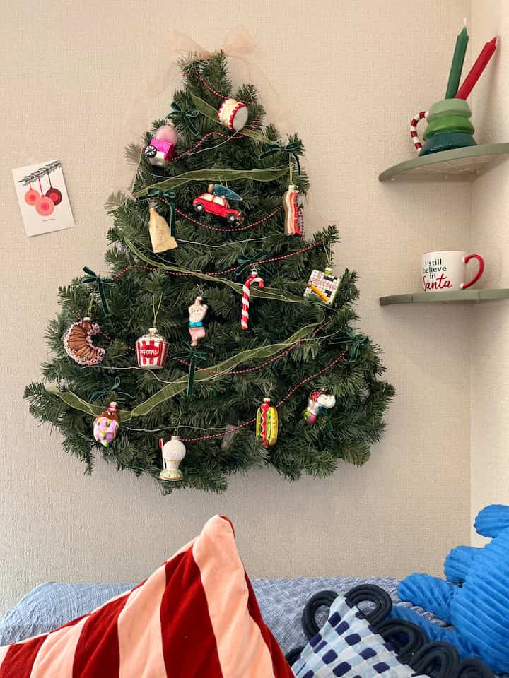 緑の壁掛けクリスマスツリーと赤のアクセントクッションがある居心地の良いリビング空間