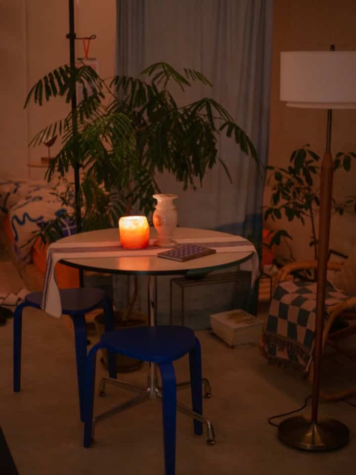 Warm natural tones and blue hues blend in a living room featuring stools and a round table with a candle creating a soft ambiance