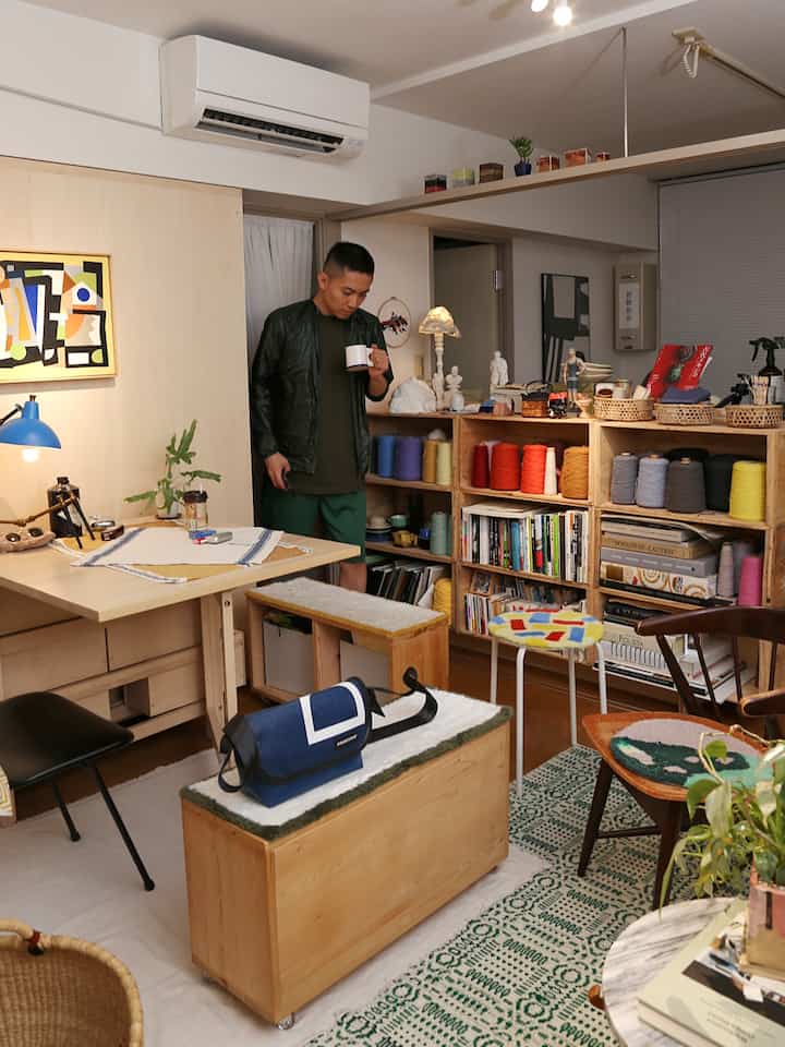 白壁と木目調の家具が調和する一人暮らしの1LDK空間、書棚とデスク、スツールが配置されたミニマルなインテリア