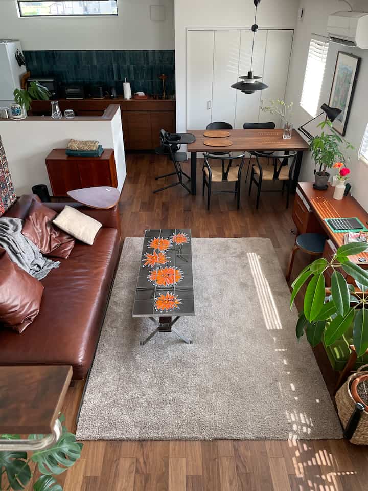 Natural modern living and dining space with white walls and wood-tone floor, brown leather sofa, and orange floral coffee table