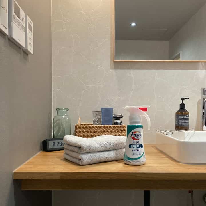 ナチュラルな色調のトイレの洗面台空間、木製テーブルとグレーのタオルが整然と配置された印象的なインテリア