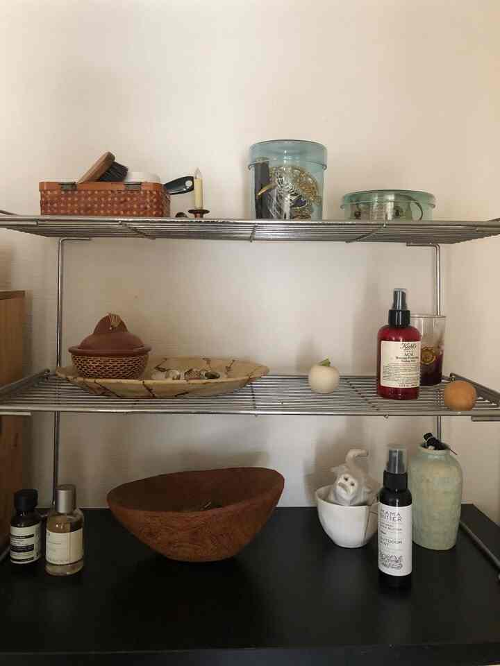 白い壁と茶色の木製アイテムが並ぶメタルシェルフ、多彩な生活雑貨とオブジェが配置された雰囲気のある玄関