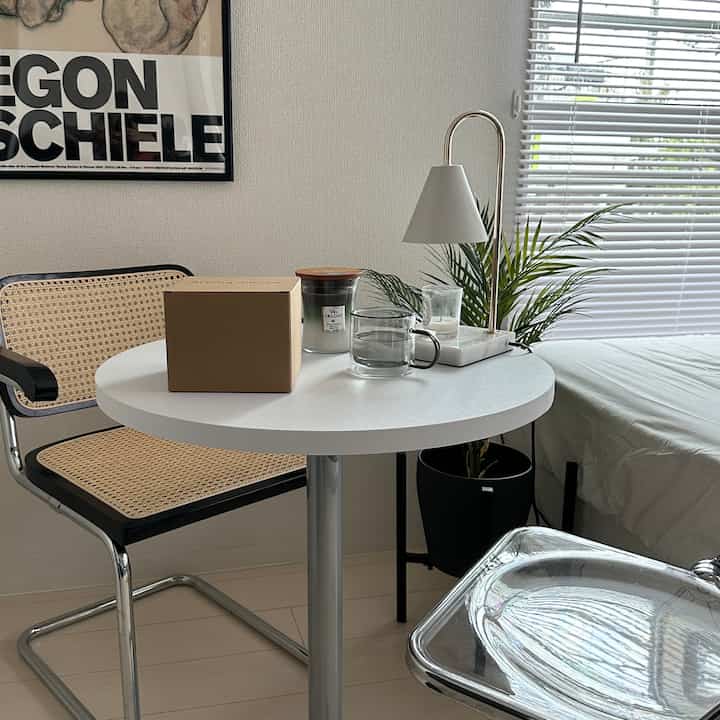 白とナチュラルカラーの寝室、丸テーブルとラタンチェア、植物と照明が配置された雰囲気のある空間