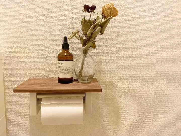 白色の壁と木目調の棚に花瓶とディフューザーが置かれた清潔感のあるバスルームのインテリア