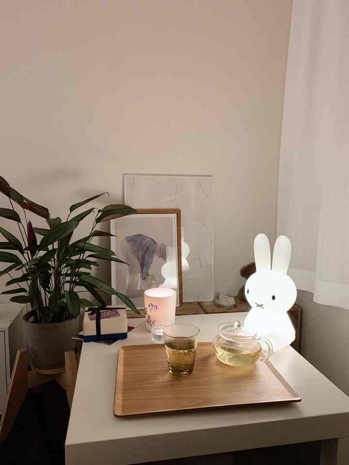 Natural-toned cozy space featuring a plant, Miffy lamp, and wooden tray with tea set on a white table