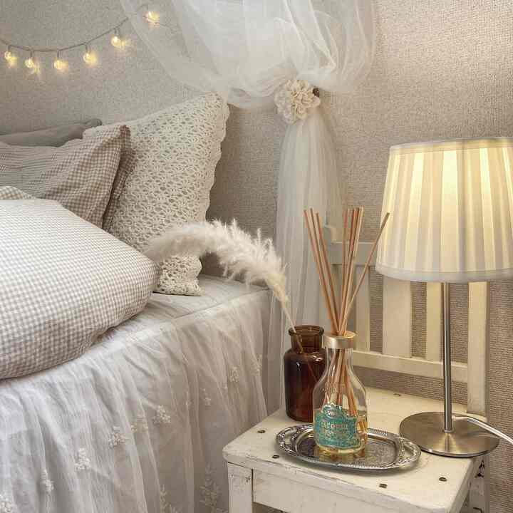 White and natural toned bedroom featuring a bed, aroma diffuser, and table lamp on the nightstand creating a cozy atmosphere