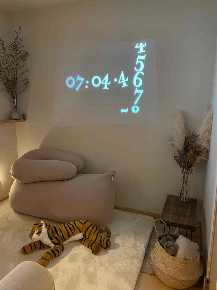 ベージュとホワイトの落ち着いたリビング、壁に時計のプロジェクション、ビーズクッションとラタンバスケット、自然素材のインテリアが配置された雰囲気のある空間