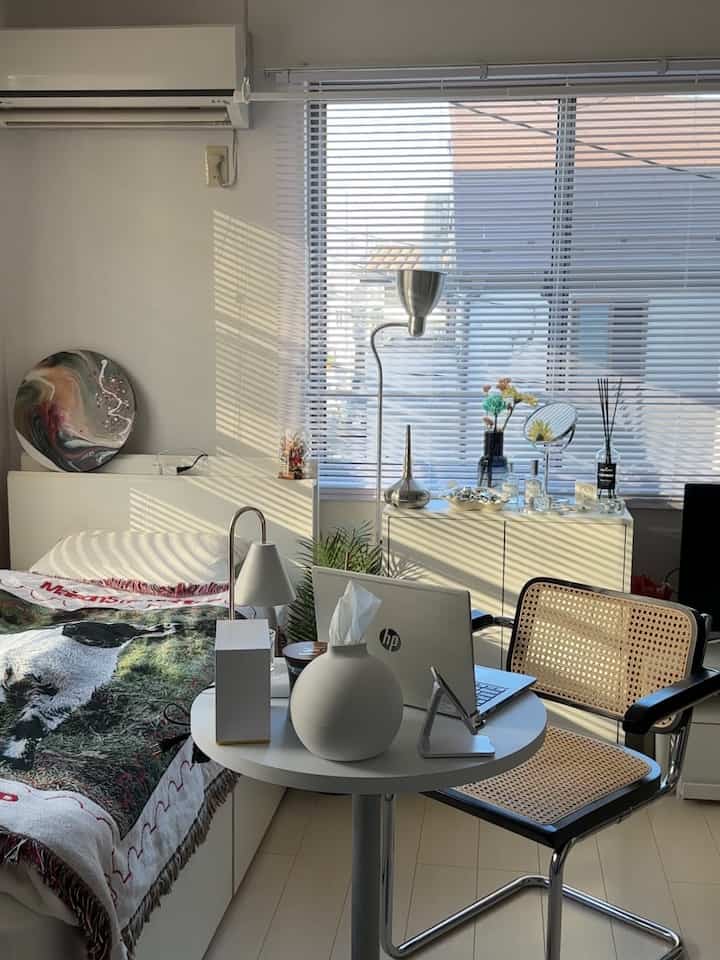 白を基調とした寝室兼作業スペース、ブラインドの影が落ちるモダンでナチュラルな雰囲気のインテリア