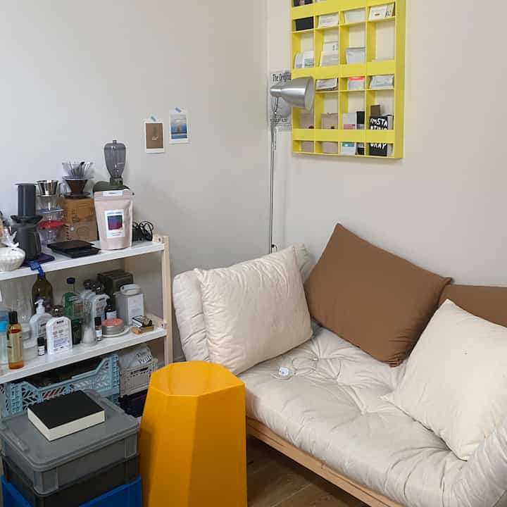 White and yellow natural tones blend in a small living room featuring a sofa bed, stool, and floor lamp in a modern setting