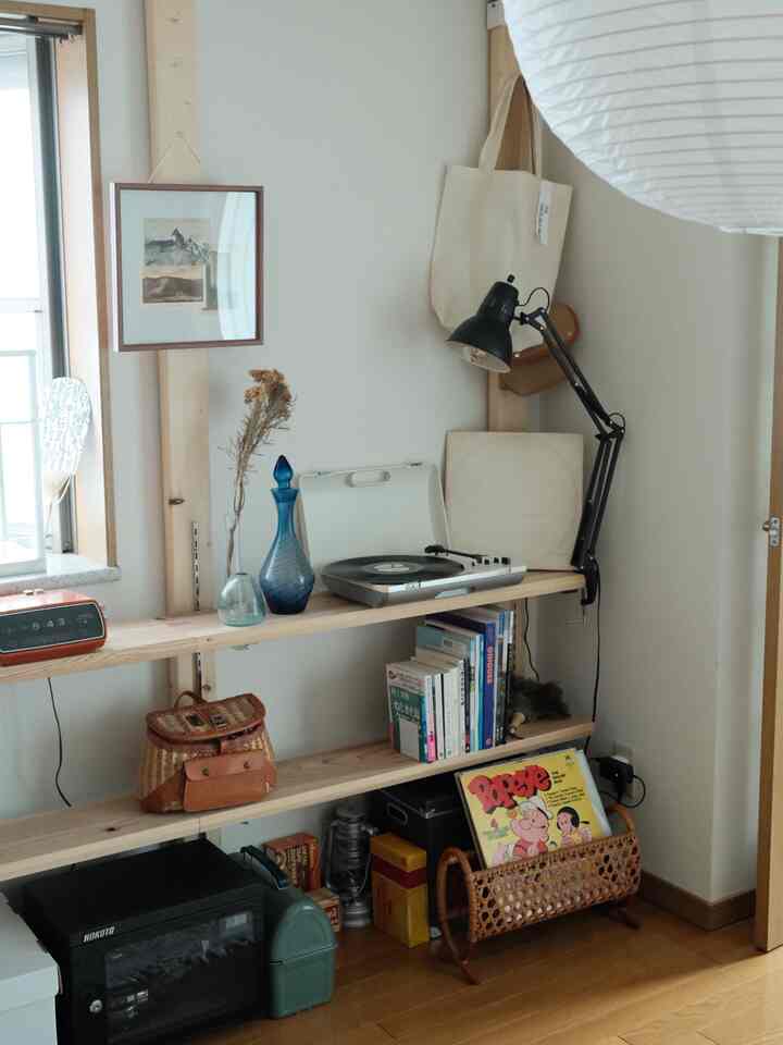 A natural-toned small room featuring wood tone shelves on the wall with retro accessories and books arranged neatly