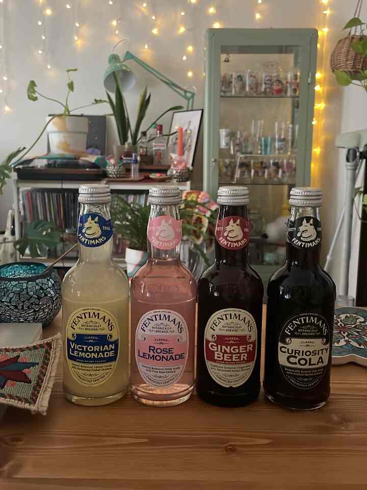 ブラウンウッドのテーブルの上に4本の飲み物の瓶が並び、背景には緑の植物とストリングライトがある雰囲気のあるホームバー空間