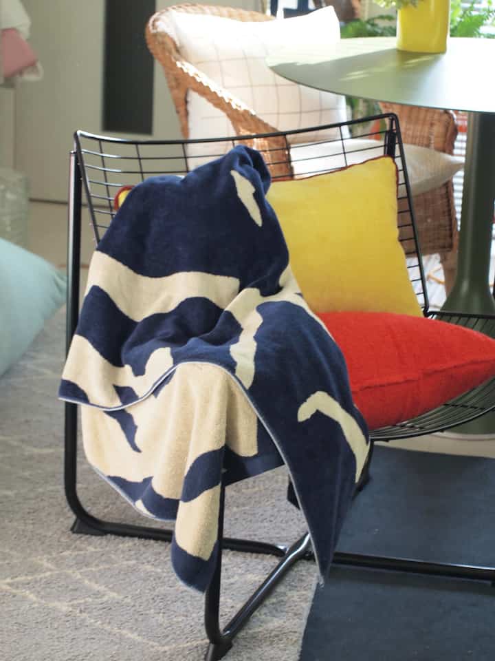 Living room with natural tones and black accents, featuring a black metal armchair with colorful cushions and a patterned blanket