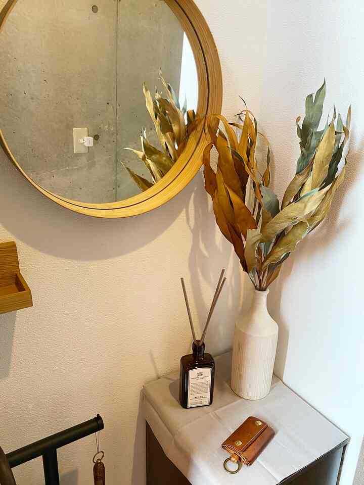 白い壁にラウンドの木製鏡とディフューザーが配置された玄関空間、ナチュラルなブラウン色調で落ち着いた雰囲気