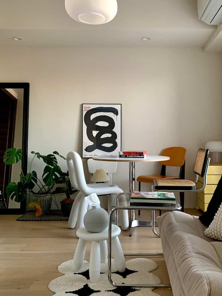 Modern dining room in white and brown tones featuring a dining table, stools, mirror, and green plants for a cozy atmosphere