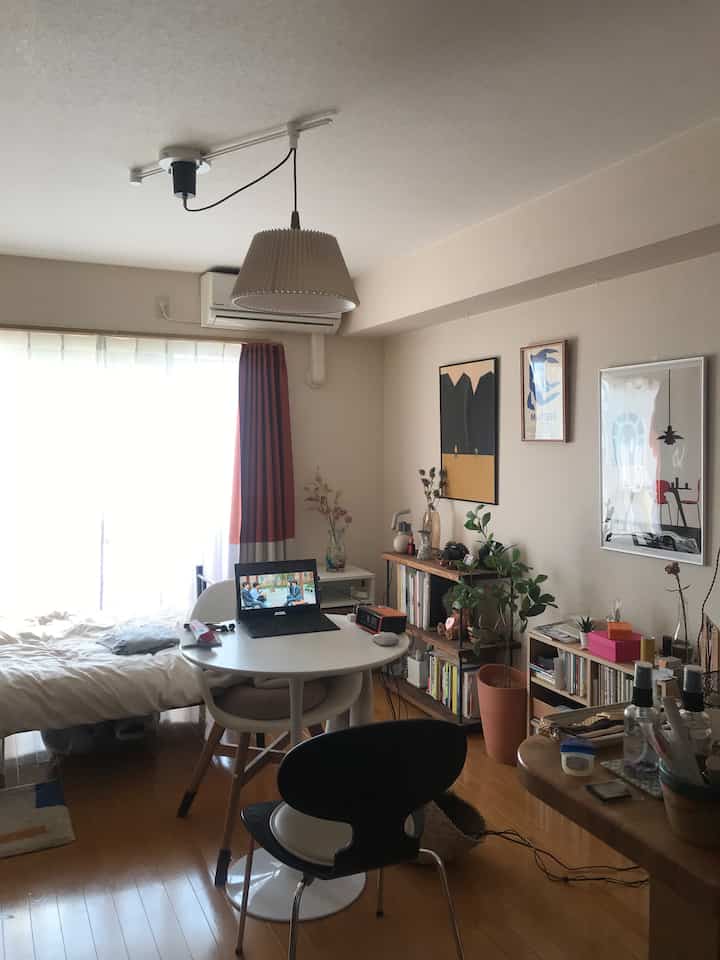 ホワイトとブラウンの落ち着いた色調のコンパクトなワンルーム、ペンダントライトとポスター、ダイニングセットが配置された雰囲気のあるインテリア