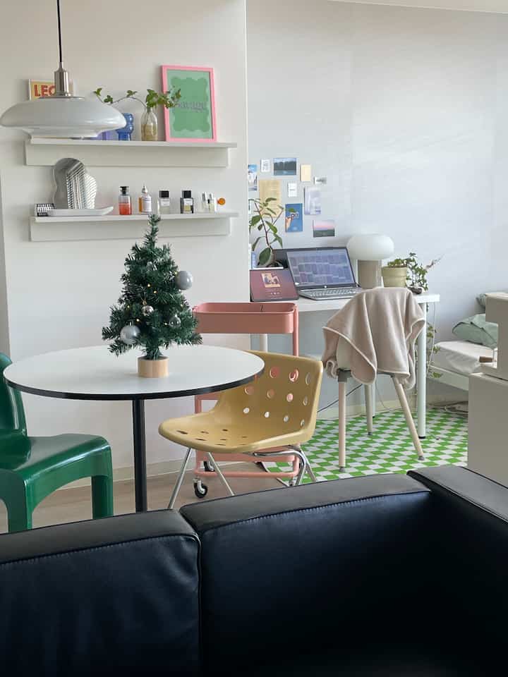 白とナチュラルトーンの壁と床、丸テーブルとカラフルな椅子が配されたリビングとホームオフィス空間