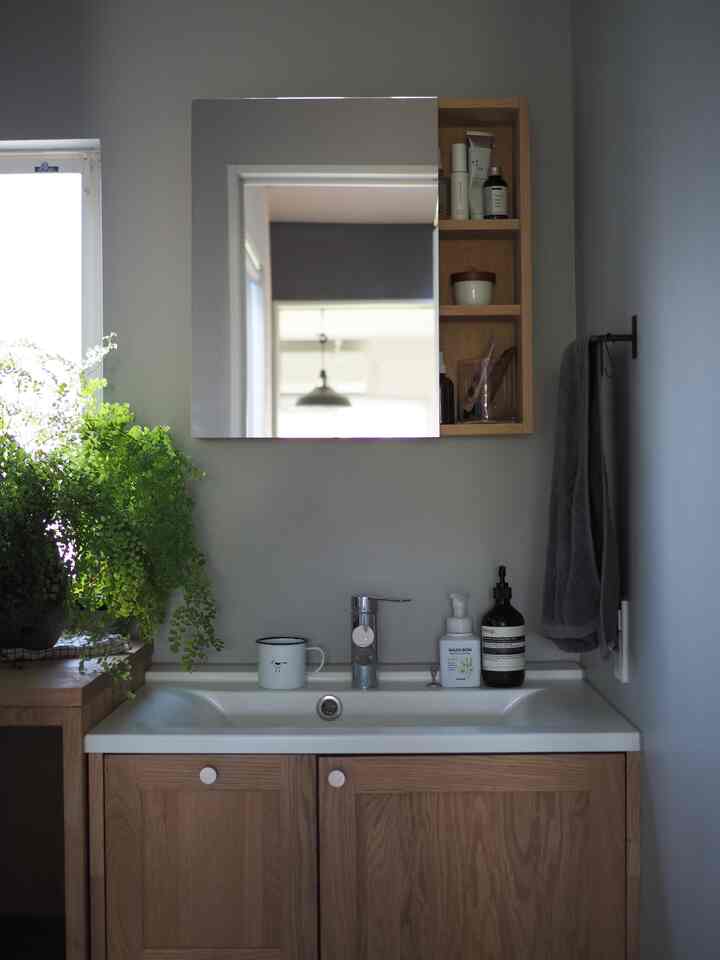 Natural color bathroom featuring wooden cabinet and open shelf, white sink and mirror with a clean and minimalist design