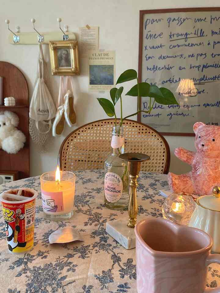 ベージュの壁と花柄テーブルクロスがあるナチュラルなリビング、ラタンチェアとキャンドル、花瓶が配置された雰囲気のあるインテリア