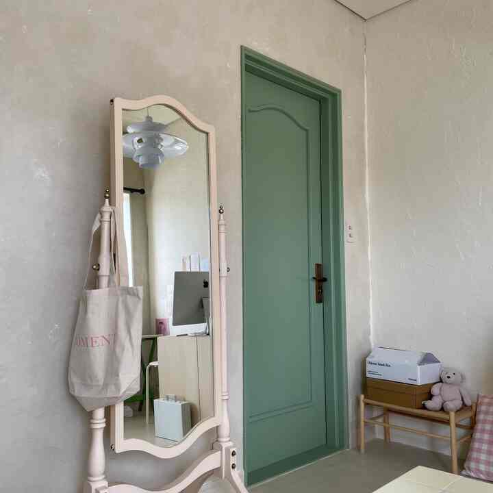 Natural modern walk-in closet with beige textured walls and light green door, featuring a large standing mirror and wooden bench in a simple setting