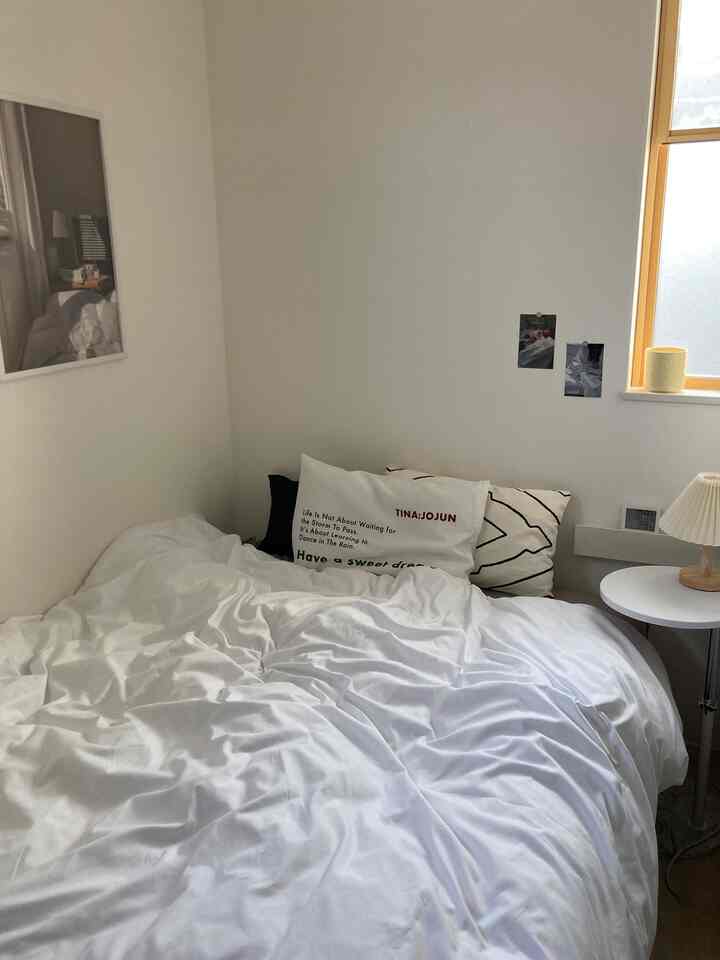 White-toned bedroom featuring white bedding and two posters, creating a neat and simple atmosphere