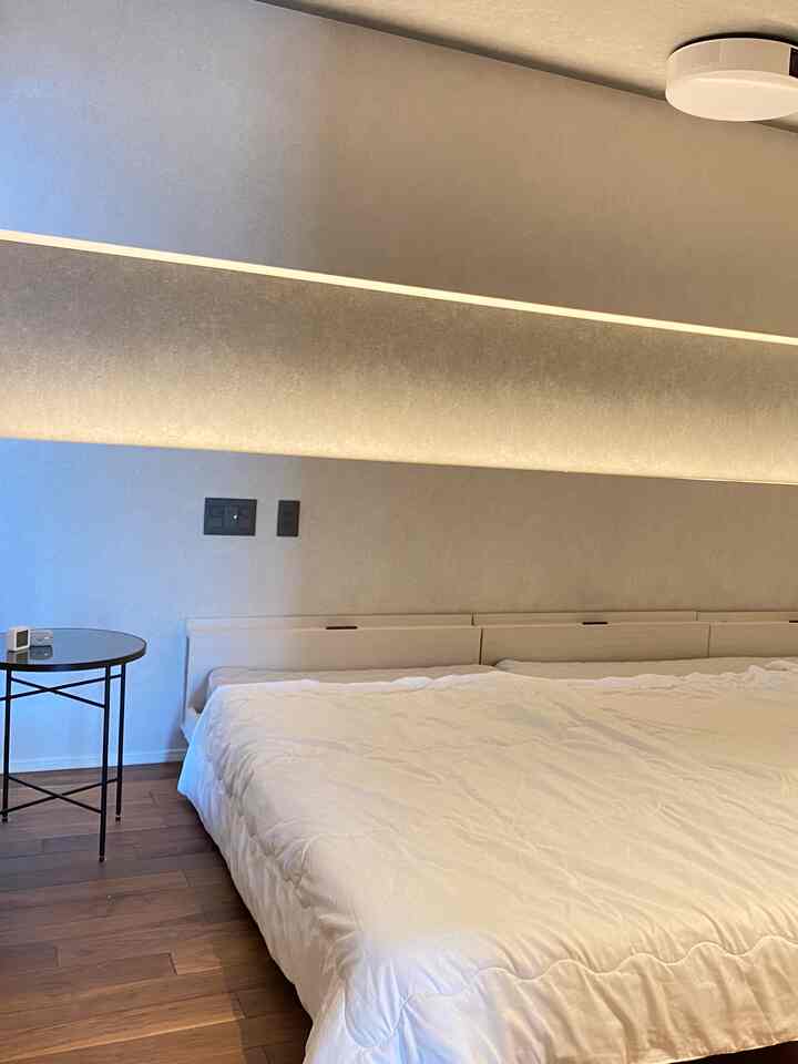 Natural wood tone bedroom with white bedding, featuring ambient indirect lighting along the wall for a cozy atmosphere