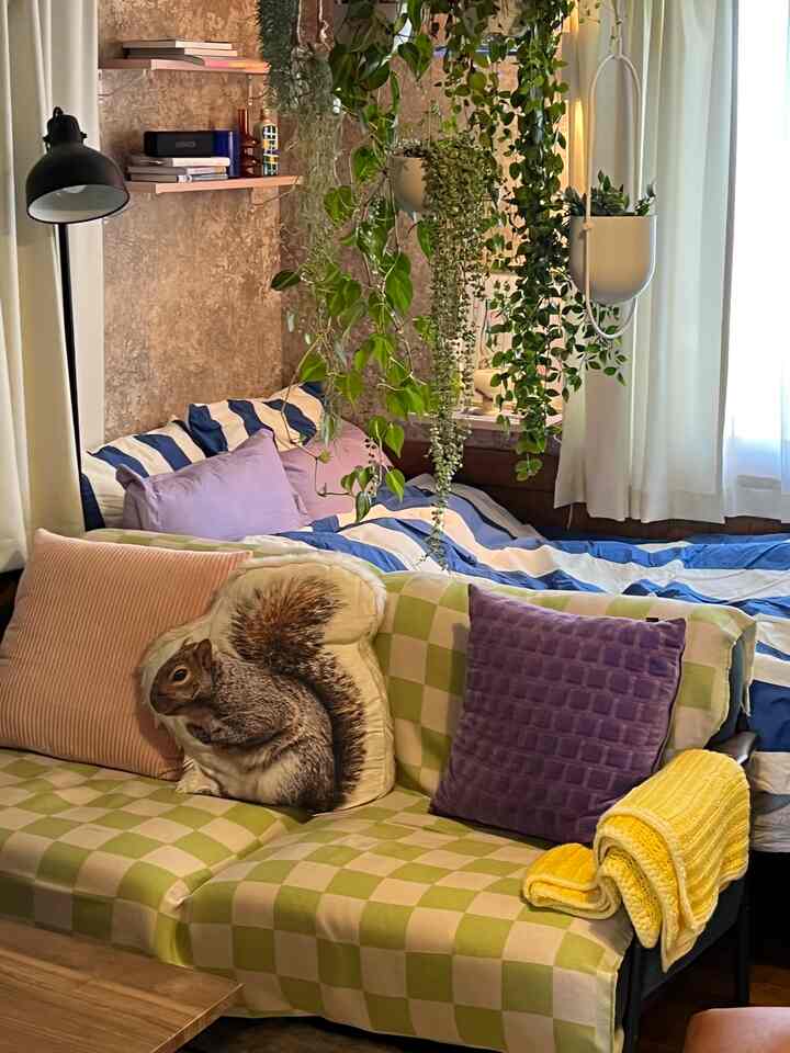 グリーンプラントとフロアランプ、チェック柄ソファ、ストライプのベッドカバーが配されたナチュラルな雰囲気の寝室