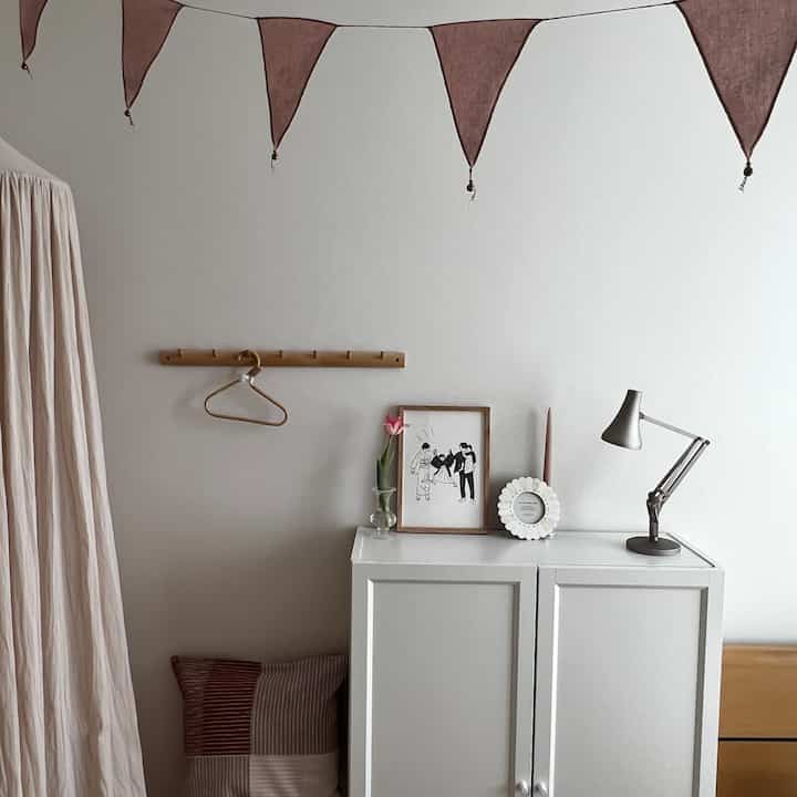 白とベージュのトーンの子供部屋、ガーランドと額縁が配置されたシンプルでナチュラルな雰囲気のインテリア