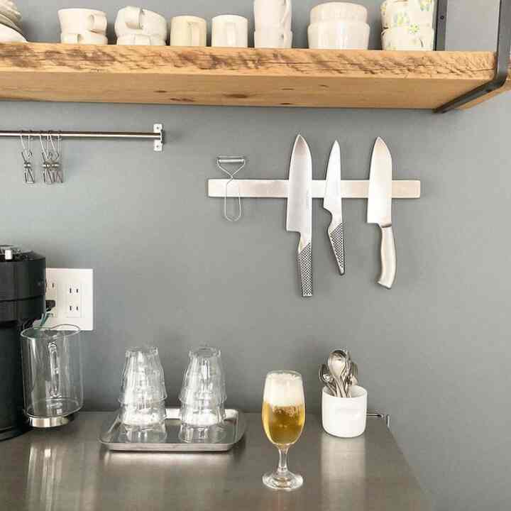 グレーの壁と木製棚があるナチュラルなキッチン、ナイフやグラス、ビールグラスが配置されたシンプルな雰囲気のインテリア