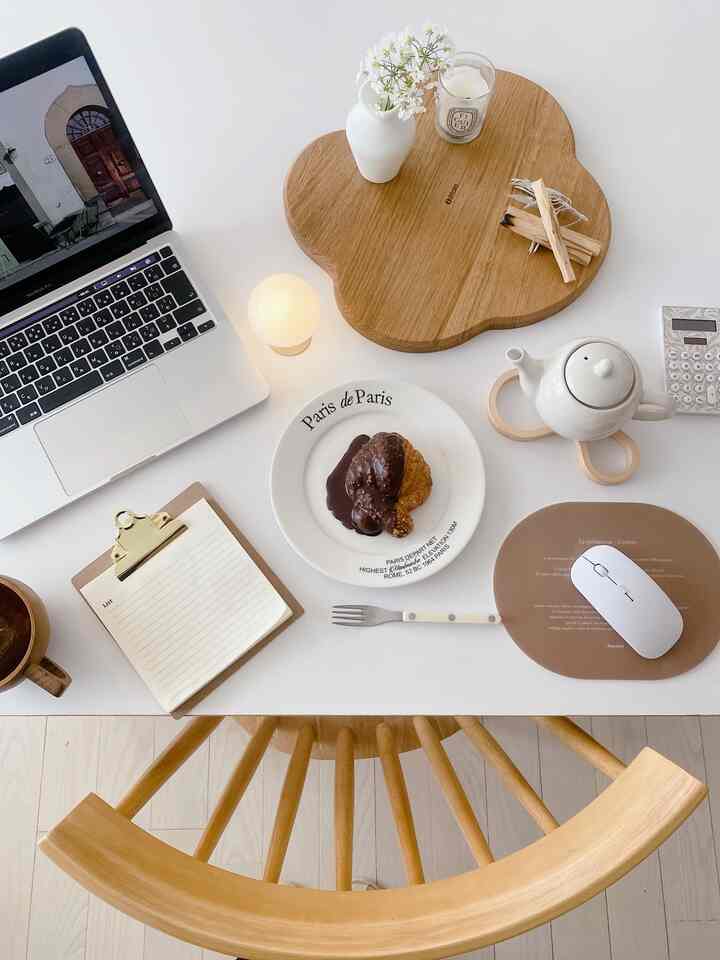 白色と木目調が調和するリビングのホームオフィス、テーブル上にラップトップと木製トレイが配置されている