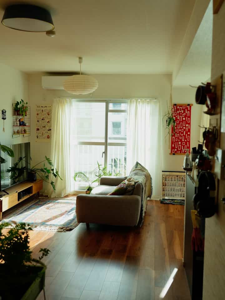 明るい自然光と木製フローリングが特徴の北欧風リビング、中央にブラウンのソファと白いペンダントライトが配置された落ち着いた空間