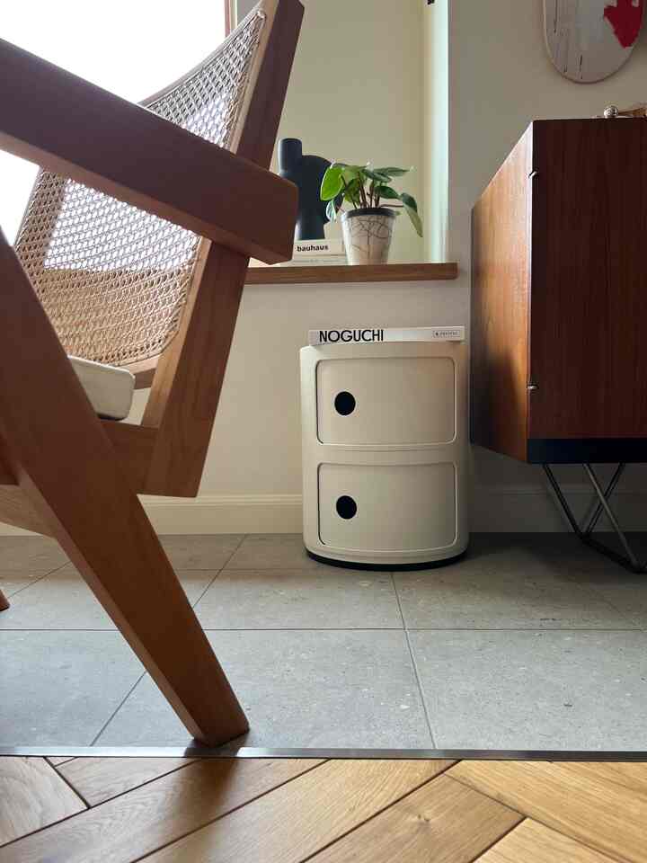 ホワイトと木目調のトーンでまとめられた小さなリビングコーナー、マットな白いチェストと木製椅子、緑の植物が配置された印象的な空間