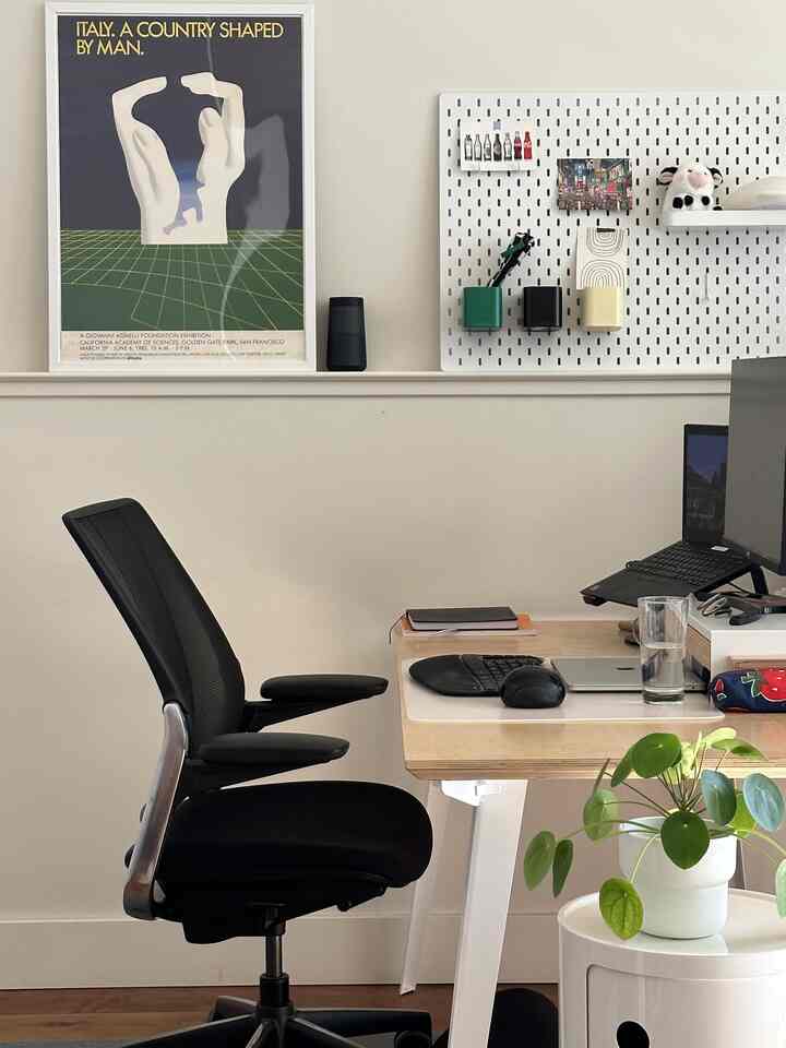 White-walled compact home office featuring a wood-tone desk, black office chair, and computer setup with a calm atmosphere
