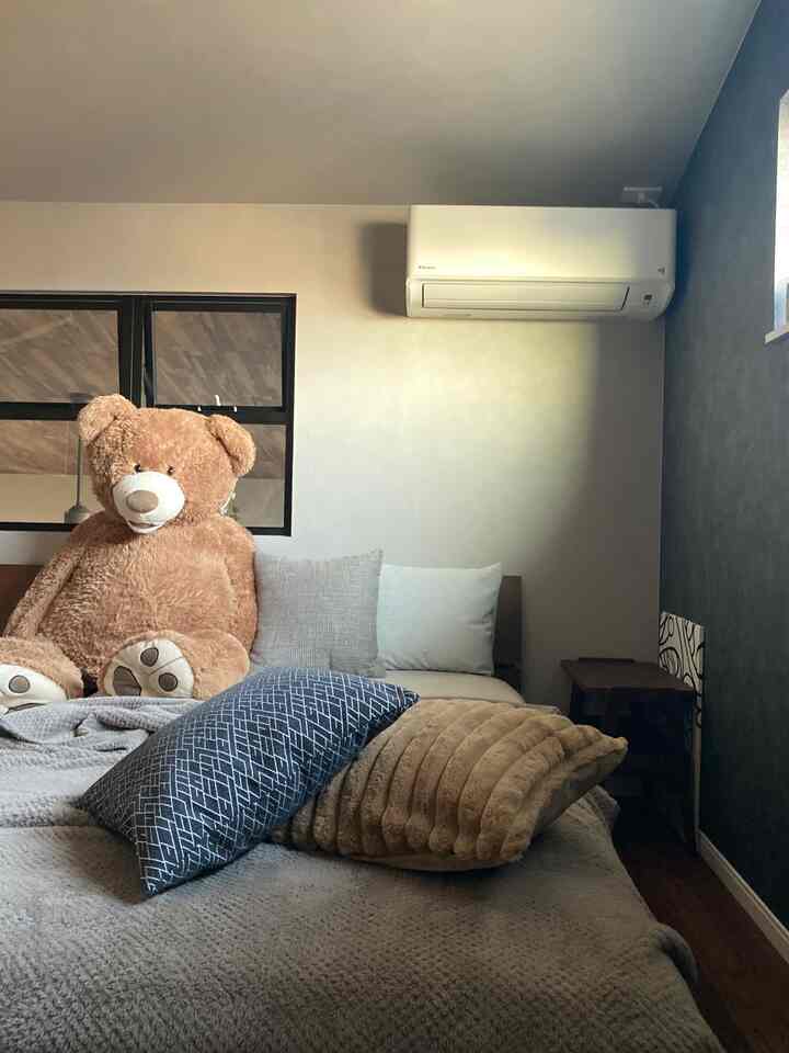 ブラウンとグレーの色調が特徴の寝室、大きなテディベアとクッションが配置された雰囲気のある空間